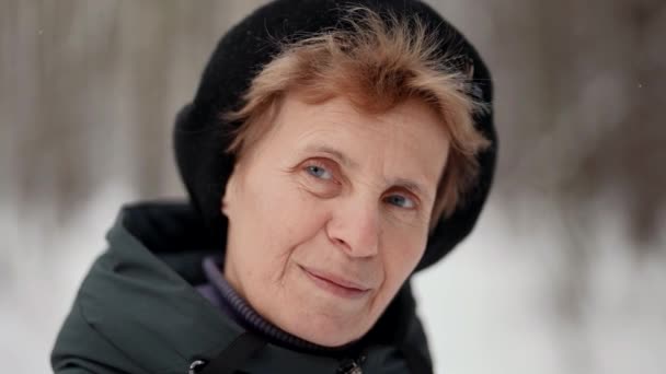 Encantador aposentado mulher está olhando para a câmera calmamente, de pé no parque no inverno, close-up retrato — Vídeo de Stock