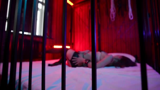 sexy Frau bewegt sich auf einem Käfigbett in einem Striptease-Club, Peep-Show mit BDSM-Themen