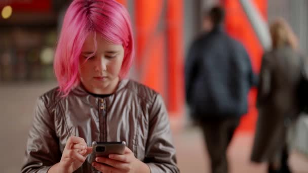 Een verdrietig tienermeisje met roze haar, dat op straat staat en berichten uitwisselt op haar smartphone. — Stockvideo