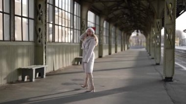 Eski tren istasyonunda kış yürüyüşü, beyaz ceketli ve bereli bir kadın geziniyor ve bankta oturuyor.