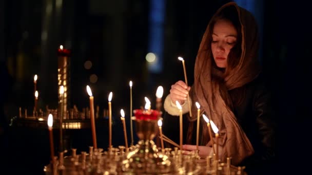 Kilisede dua eden genç bir kadın, Ortodoks ya da Katolik tapınaklarında mumların önünde duruyor. — Stok video