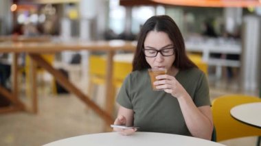 Yetişkin bir kadın kafede latte içiyor ve akıllı telefonuyla internette sörf yapıyor.
