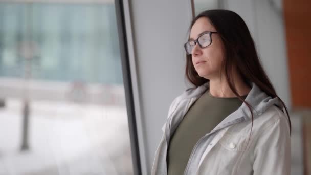 Affascinante donna di mezza età con gli occhiali sta visualizzando in una grande finestra durante il giorno in inverno — Video Stock