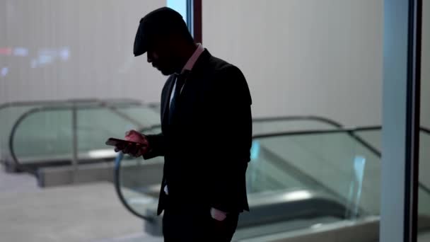 Силует людини в костюмі з мобільним телефоном проти світлового залу підземної станції — стокове відео
