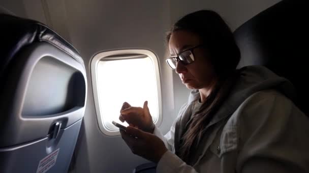 Жінка використовує смартфон всередині літака під час польоту, подорожуючи літаком — стокове відео