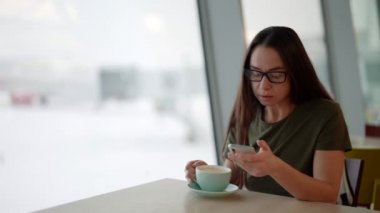 Yetişkin bir kadın akıllı telefonla mesaj gönderiyor ve okuyor. Kafede oturuyor.