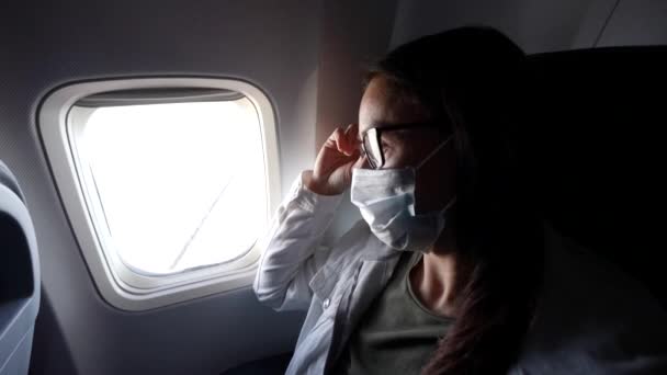 Mulher com máscara facial médica está viajando de avião, sentado dentro da cabine no assento da janela — Vídeo de Stock