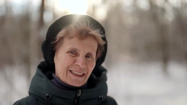 Souriant vieille femme est debout seul dans la rue dans le parc dans la journée d'hiver, en regardant la caméra calmement — Video