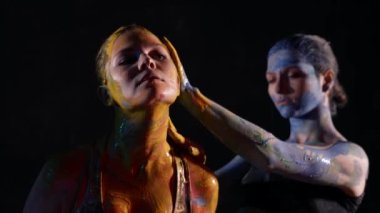Parlak resimlerle çağdaş sanat performansları, bayanlar dans ediyor ve cesetlerin üzerine boya sürüyor.