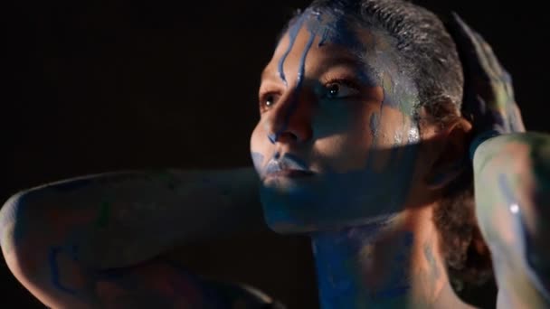 Пристрасна дама з синіми фарбами на шкірі погладжує голову, портрет у темній кімнаті — стокове відео