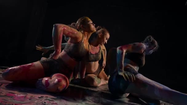 Tancerki współczesne kobiety wykonują taniec artystyczny w ciemnej scenie z farbami na podłodze — Wideo stockowe