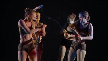 Güzel genç kadınlar vücut sanatı için boyalarla oynuyorlar, cilde su sıçratıyorlar ve gülüyorlar.