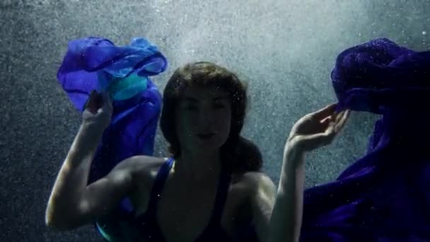 Lenyűgöző és titokzatos hölgy kék selyem ruhában lebeg a mélységben, víz alatti portré — Stock videók