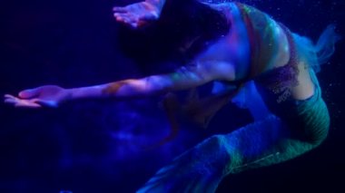 Balık kuyruklu su perisi koyu mavi bir derinlikte yüzüyor, sanat ve fantezi sahnesi.