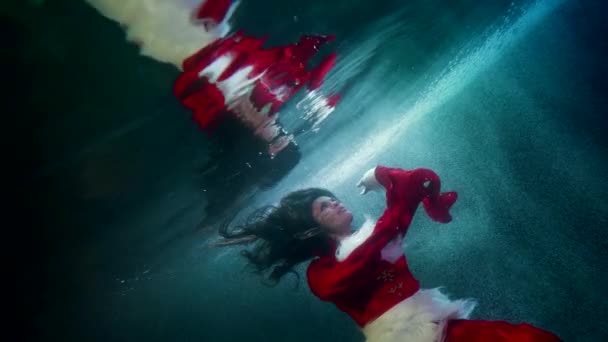 Очаровательная женщина под водой, касаясь поверхности воды замерзшей реки или озера, красивая дама в красном — стоковое видео
