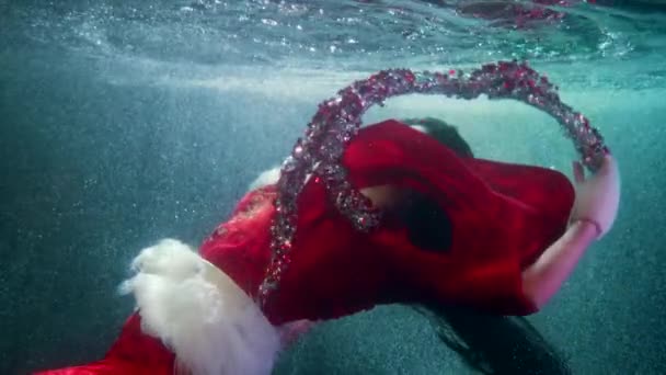 Suyun altında Noel Masalı, kırmızı elbiseli kadın süslerle oynuyor ve derinlerde yüzüyor. — Stok video