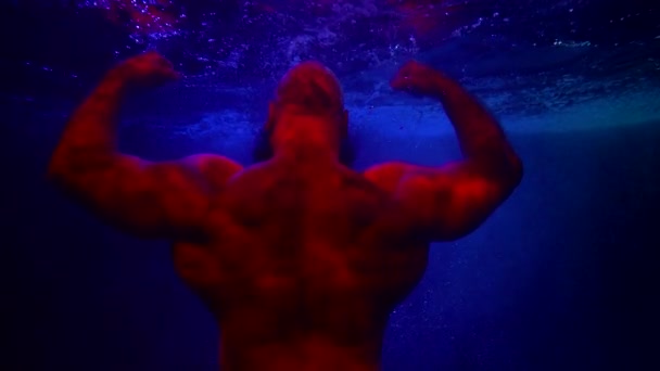 Suyun altında güçlü kaslı adam, kaslı sırtında dikiz, mavi suya karşı kırmızı siluet. — Stok video