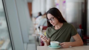 Havaalanı kafesinde esmer bir kadın cep telefonuyla sohbet ediyor ve uçağa binmeyi bekliyor.