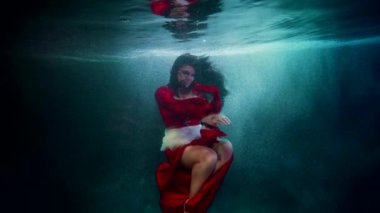 Kırmızı elbiseli gizemli kadın figürü okyanusun derinliklerinde yüzüyor. Suda sıradışı bir kadın portresi.