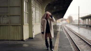 Genç ve çekici sarışın kadın yağmurlu bir günde tren istasyonunda tek başına yürüyor.