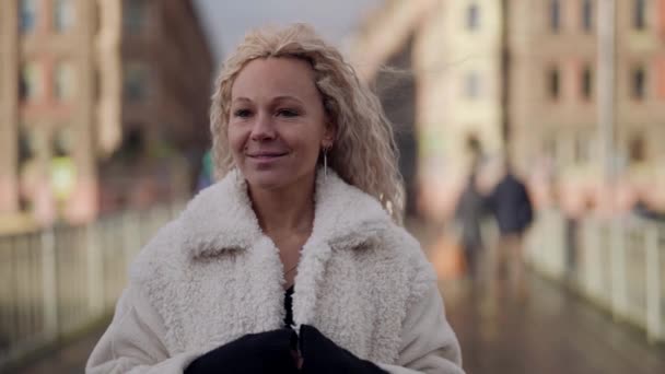 Mulher bonita com cabelo loiro estendido está andando na rua da cidade em dia frio ensolarado, retrato — Vídeo de Stock