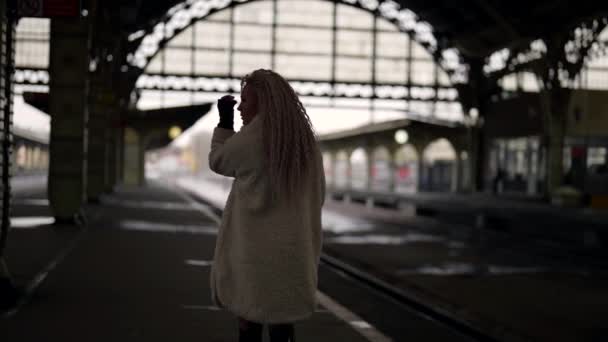 Блондинка ходит одна на старом железнодорожном вокзале, в пригороде города — стоковое видео