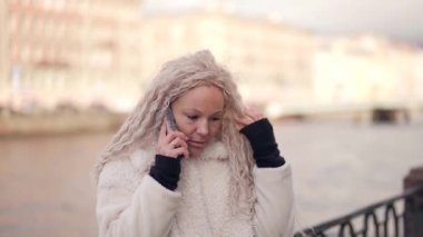 Sarışın kadın caddede cep telefonundan arıyor ve kamerayla flört ediyor.