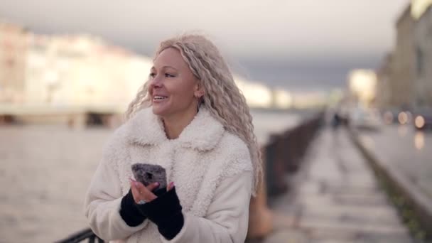 Trendig blond kvinna svarar på mobilsamtal utomhus, promenader ensam i stadsbanken — Stockvideo