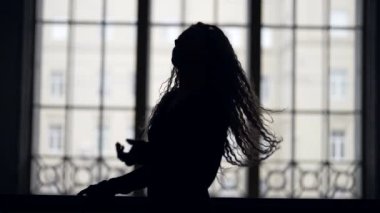 Uzun saçlı romantik, ince bayan geniş pencereye poz veriyor, siluet fotoğraf.