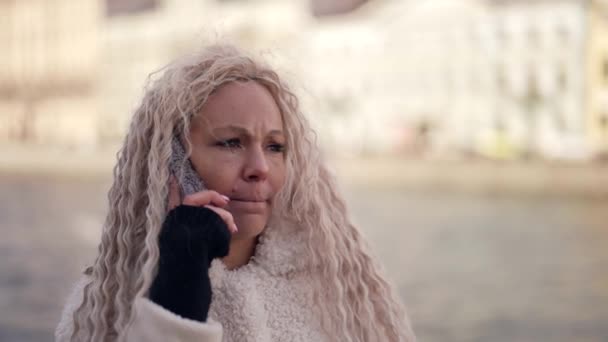 Sad and annoyed woman is talking by mobile phone on street in cold day, quarreling with someone — Stock Video