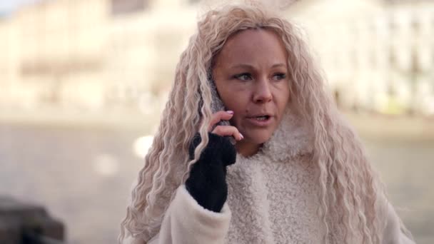 Stressed woman is talking by mobile phone on city street, closeup portrait of emotional face — Stock Video