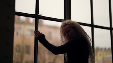 Seksi sarışın bayan sonbaharda çatı katında büyük pencerelerin yanında poz veriyor.