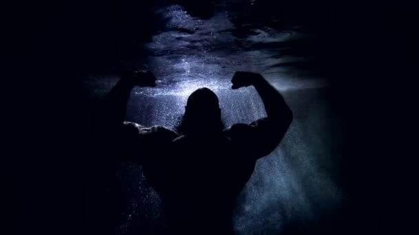 Επική ανδρική φιγούρα σε σκοτεινό βάθος της θάλασσας, ισχυρό bodybuilder δείχνει τους μυς των χεριών του — Αρχείο Βίντεο