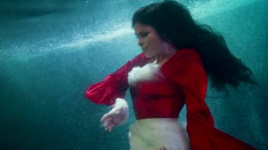 Güzel esmer kadın denizin ya da nehrin derinliklerinde yüzüyor. Su altında ağır çekim.