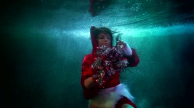 Kırmızı elbiseli muhteşem elf kadın suyun altında yüzüyor ve süs, Xmas teması ve peri masalıyla oynuyor.
