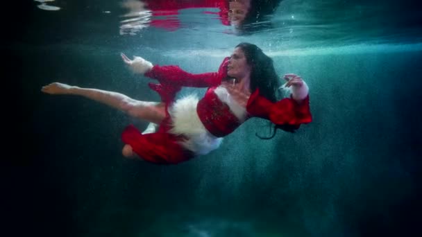 Okouzlující štíhlá žena v červených šatech se vznáší ve vodě bazénu, pohádka a fantasy záběr — Stock video