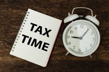 Tahta masadaki not defterinde Vergi Zamanı yazan çalar saat. işletme muhasebe ödeme tarihi vergisi.