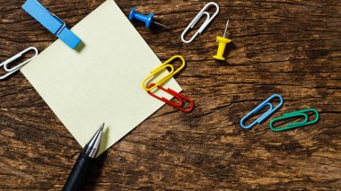 Ahşap ofis masasında kalem iğnesi ve ataç kağıdı olan boş yapışkan not kağıdı. 