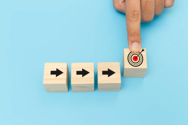 Ok ve hedef sembolleri olan tahta küp bloklar, hedef simgelerini işaret eden insan elleri hedef simgesi olan tahta küpleri işaret ediyor. derecelendirme ve sıralama iş konsepti.