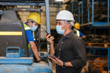Mühendis adam yüz maskesi takıyor. Depoda çalışmak için telsiz ve tablet tutuyor. işyeri fabrikası endüstriyel ağır makine.