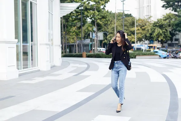 美丽的亚洲女商人穿着黑色西服 会讲电话 走在城市街道上 复制文本词的空间使用 — 图库照片