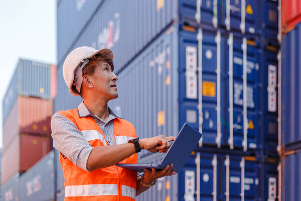 man engineering in uniform wearing safety helmet using laptop checking containers loading. Area logistics import export and shipping.