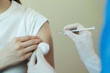 Maske takan kadın doktor elinde şırıngayla hastaya koruma için aşı veriyor. COVID-19 salgını sırasında. Doktorlar salgın sırasında hastaları aşılarlar..