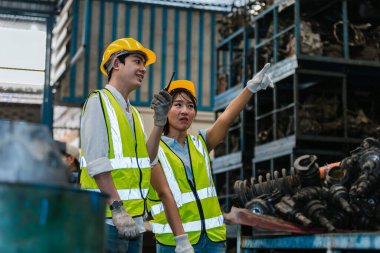 Ekip mühendisleri, işçiler üniforma giyer ve yedek parça deposunda kask hakkında konuşur. Erkek ve kadın işyeri fabrikası endüstriyel ağır makine.