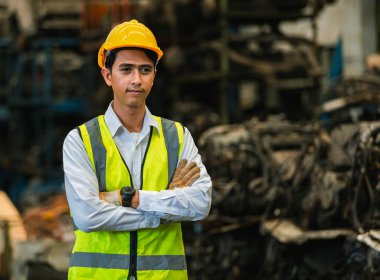Asyalı mühendis portresi üniforma giyer ve depoda kask takar. Fabrika makinelerinde çalışan erkek işçi. iş yeri ağır sanayi.