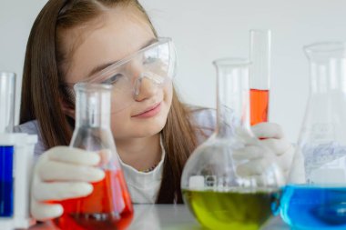 Çocuk bilim öğrencileri, beyaz laboratuvar odasında sıvı kimyasal deneyler üzerinde çalışıyorlar. Öğrenci kız elinde biyo-teknoloji ile test tüpü tutuyor. Bilim eğitimi kavramı.