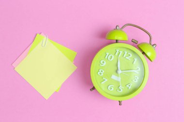 Pembe arka planda not notu olan yeşil alarmlı saat. anımsatıcı planlayıcı konsepti.