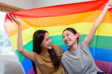 Gay bayrağıyla mutlu Asyalı homoseksüel kız. Lezbiyen çift, sembolik ifade bayrağı. Homoseksüel çift birbirine sarılıyor..