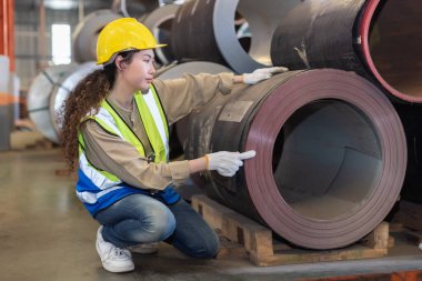  Asyalı kadın işçiler fabrikada demir üretimini kontrol etmek için kırmızı kask takıyorlar. Ağır endüstriyel imalat işyeri. Kadın mühendis profesyonel makine atölyesi.