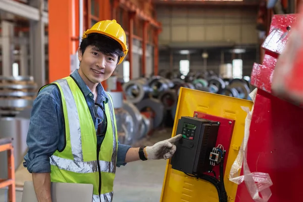 asian man engineer technical department using laptop working in power plant control panel of industry factory. male professional system electrician machine control with computer laptop.